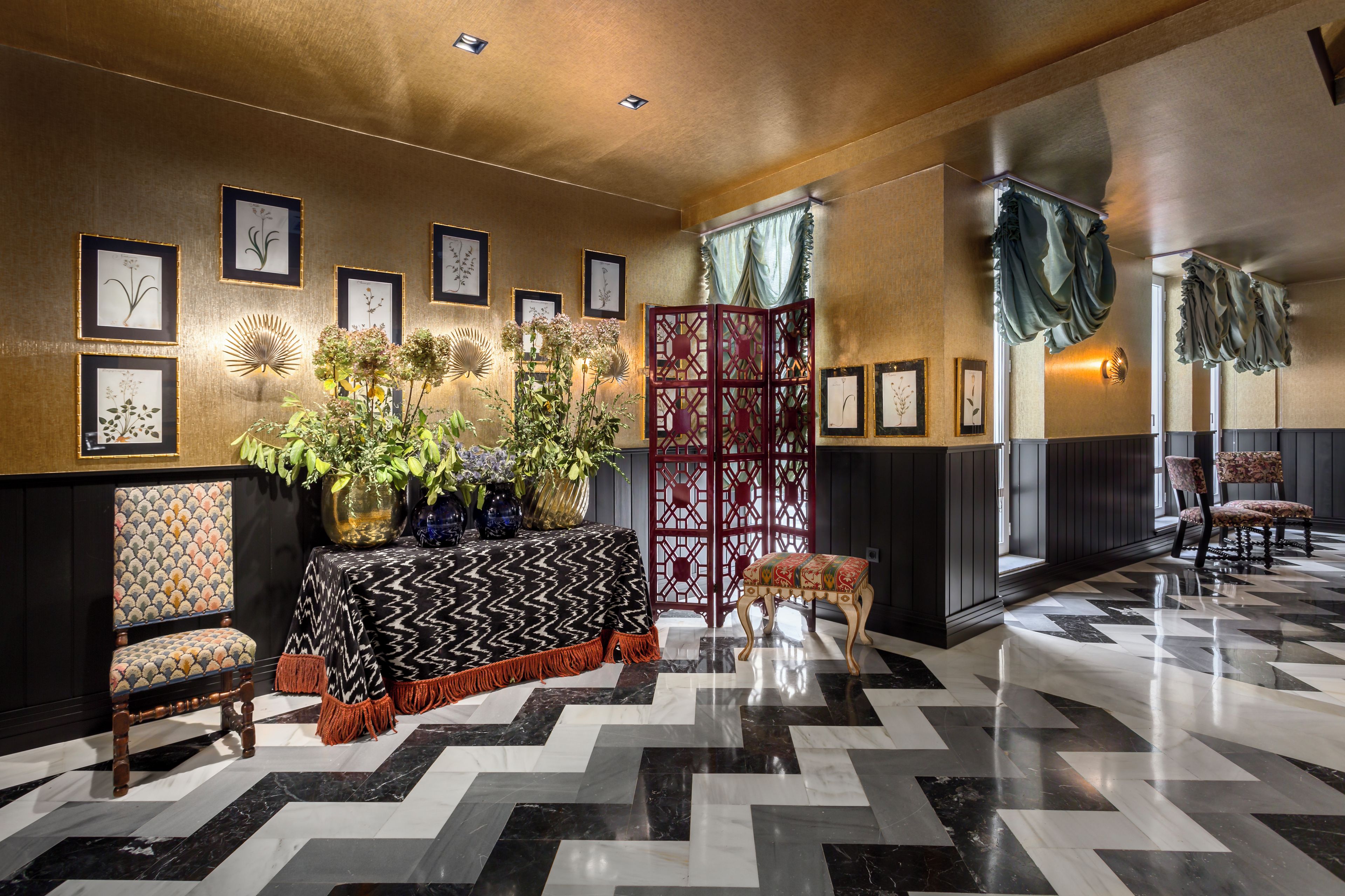 Una hall d'hotel con pavimento a motivi, una reception con tovaglia decorata, stampe botaniche incorniciate al muro e un'elegante composizione floreale.
