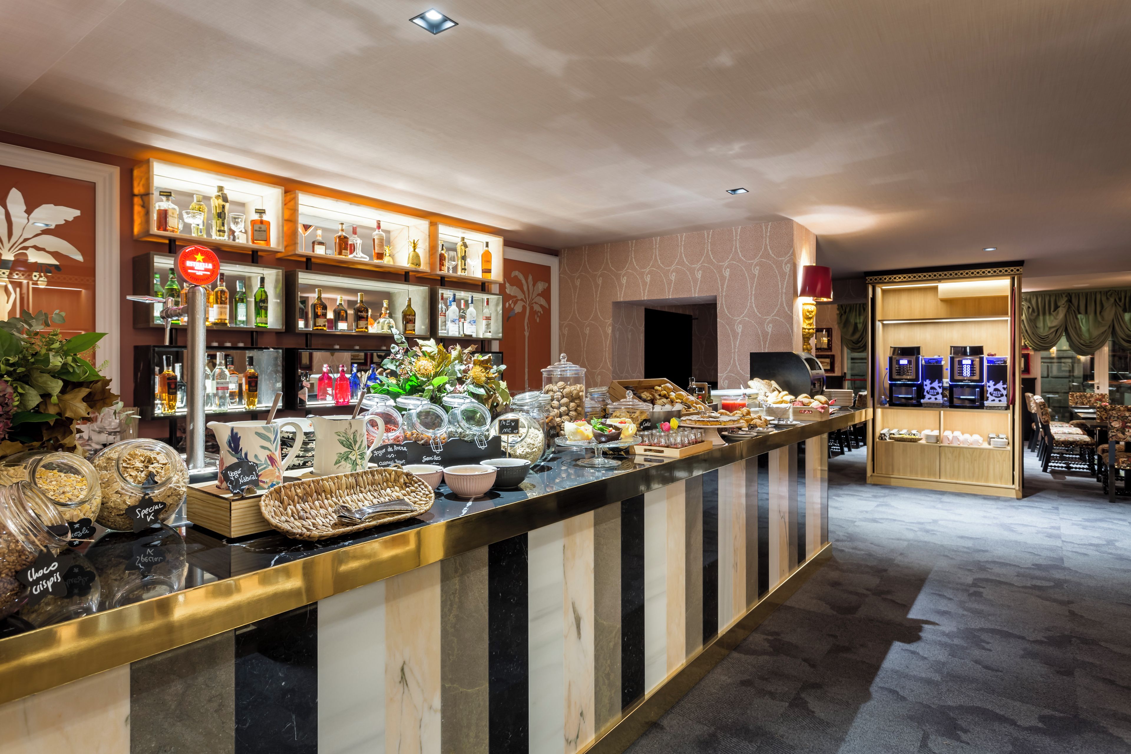 Un bar de hotel con diversas bebidas y aperitivos, una zona de estar con sillas y vistas a la calle.
