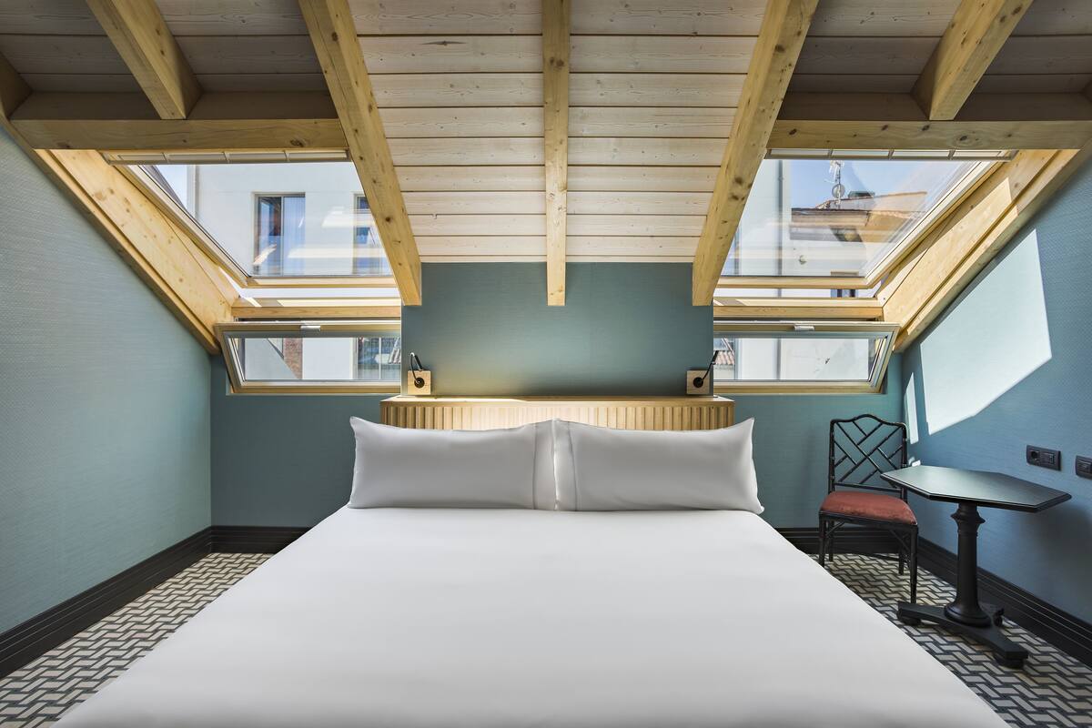 Ein Schlafzimmer mit einem großen Bett, Dachfenstern, einem kleinen Tisch und einem Stuhl.