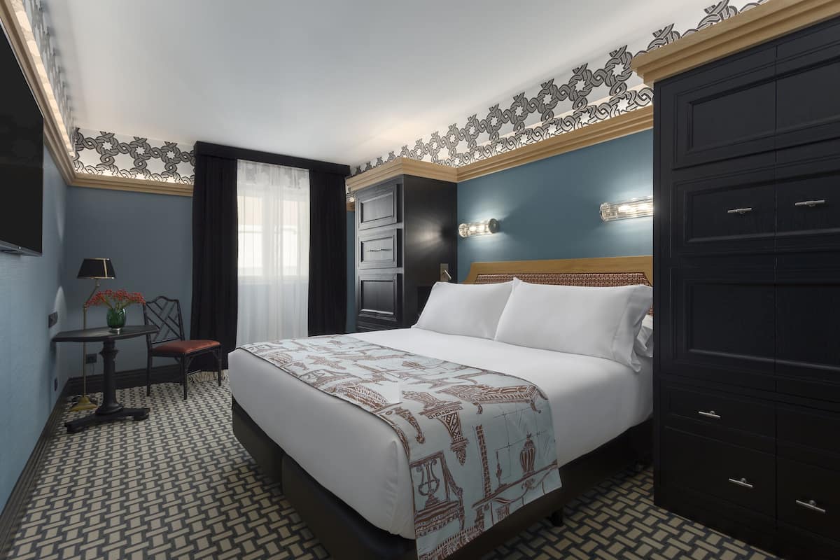 Ein Hotelzimmer mit einem großen Bett, einem Schreibtisch mit Lampe, einem Stuhl und einem Kleiderschrank.
