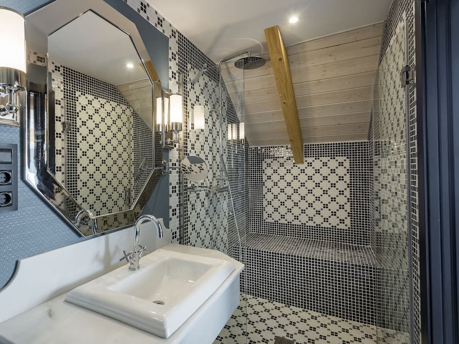Un baño con lavamanos blanco, un espejo grande y paredes de azulejos con un diseño en blanco y negro.