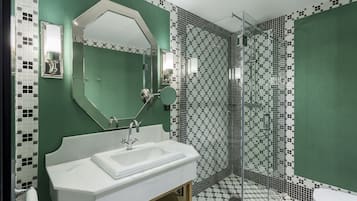 Une salle de bain avec un lavabo blanc, un grand miroir et une douche dotée d’une porte en verre.