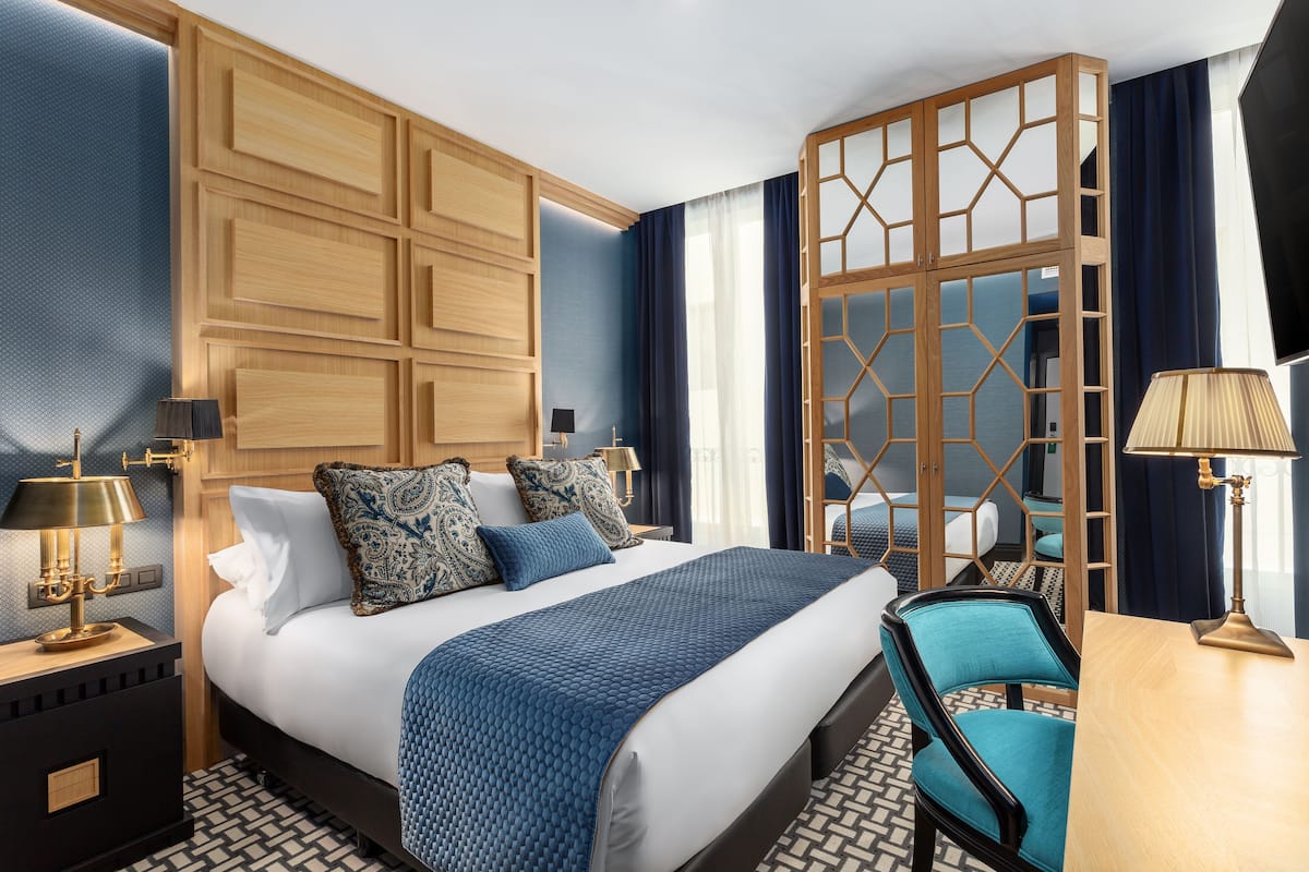 Ein modernes Hotelzimmer mit einem großen Bett, einem Holzschrank, einem Schreibtisch und einem Sessel.
