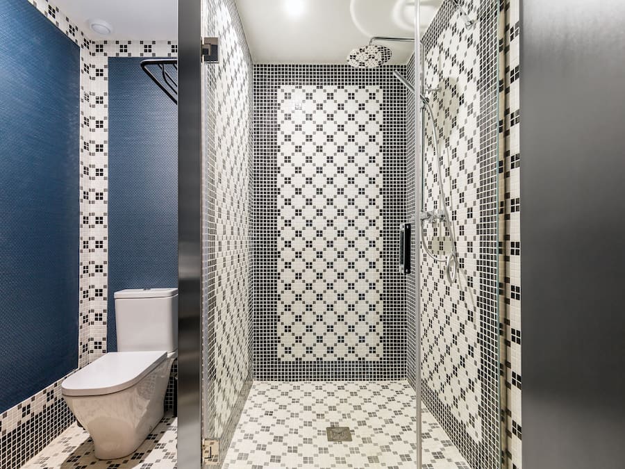 Un baño con pared azul, inodoro blanco y zona de ducha con piso de baldosas estampadas.