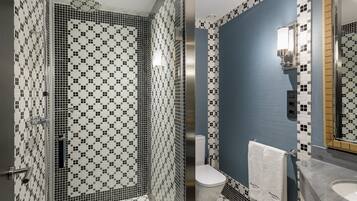 A bathroom with a shower area featuring mosaic tile walls and a toilet with a towel hanging on the wall.