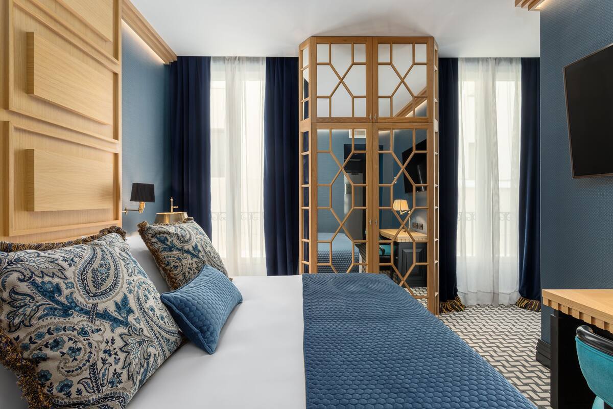 Ein modernes Hotelzimmer mit einem großen Bett, einem Holzschrank, einem Schreibtisch und Blick durch eine Raumtrennung.