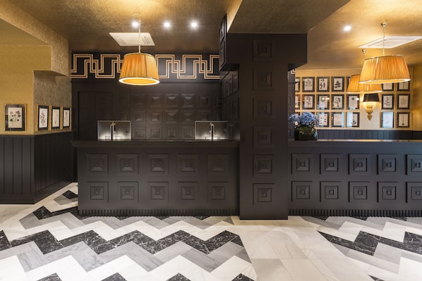 Un área de bar moderna con diseños geométricos en la pared, iluminación colgante y un suelo estampado.