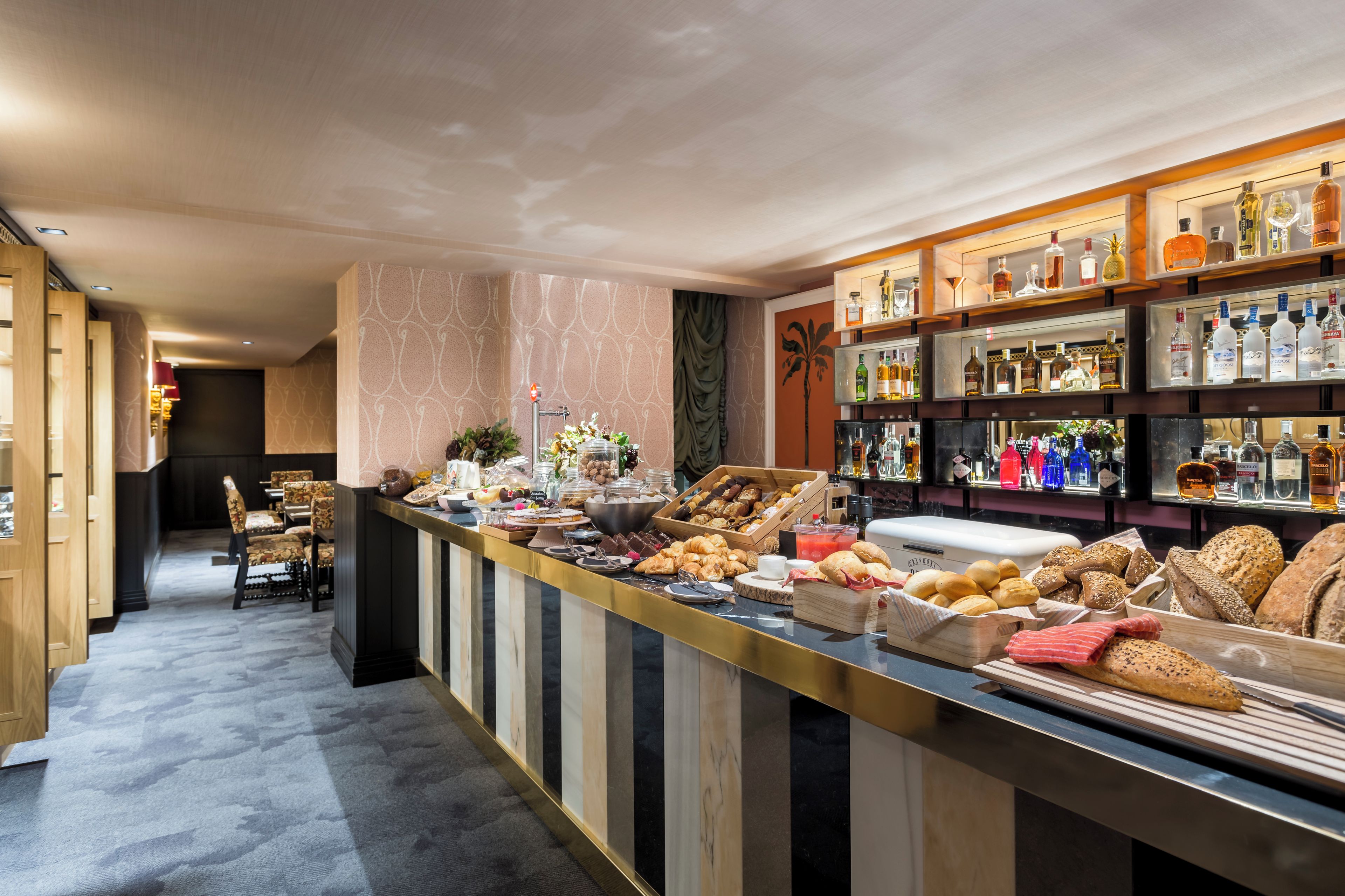 Zona de bar con diversas opciones de comida y bebida, incluyendo pan, pasteles y botellas de licor.
