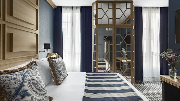 Een hotelkamer met een groot bed, een houten garderobe, een bureau met lamp en uitzicht op de stad.
