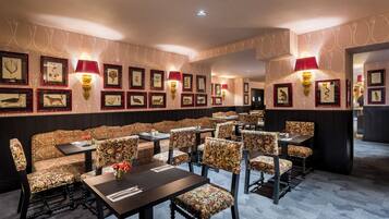 A restaurant with patterned upholstered booths and tables, framed artwork on the walls, and wall-mounted lamps.
