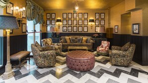 Een kamer met een zithoek, een voetenbankje en gestreept fauteuils, met ingelijste botanische prints aan de muur.