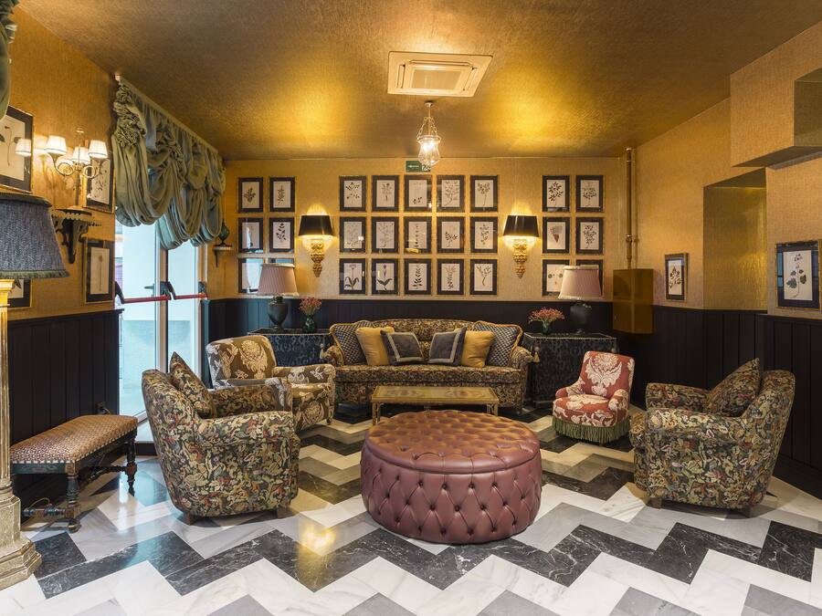 A room with a sofa set, ottoman, and patterned chairs, with framed botanical prints on the wall.