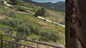 Vista desde una ventana sobre un paisaje montañoso con una carretera, vegetación y colinas al fondo.