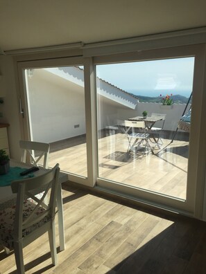 Una habitación con una puerta corrediza de vidrio que da a un patio exterior. En el interior, hay una mesa con sillas y una pequeña planta en maceta.