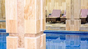 Un área de piscina con sillones de descanso y piso de baldosas.