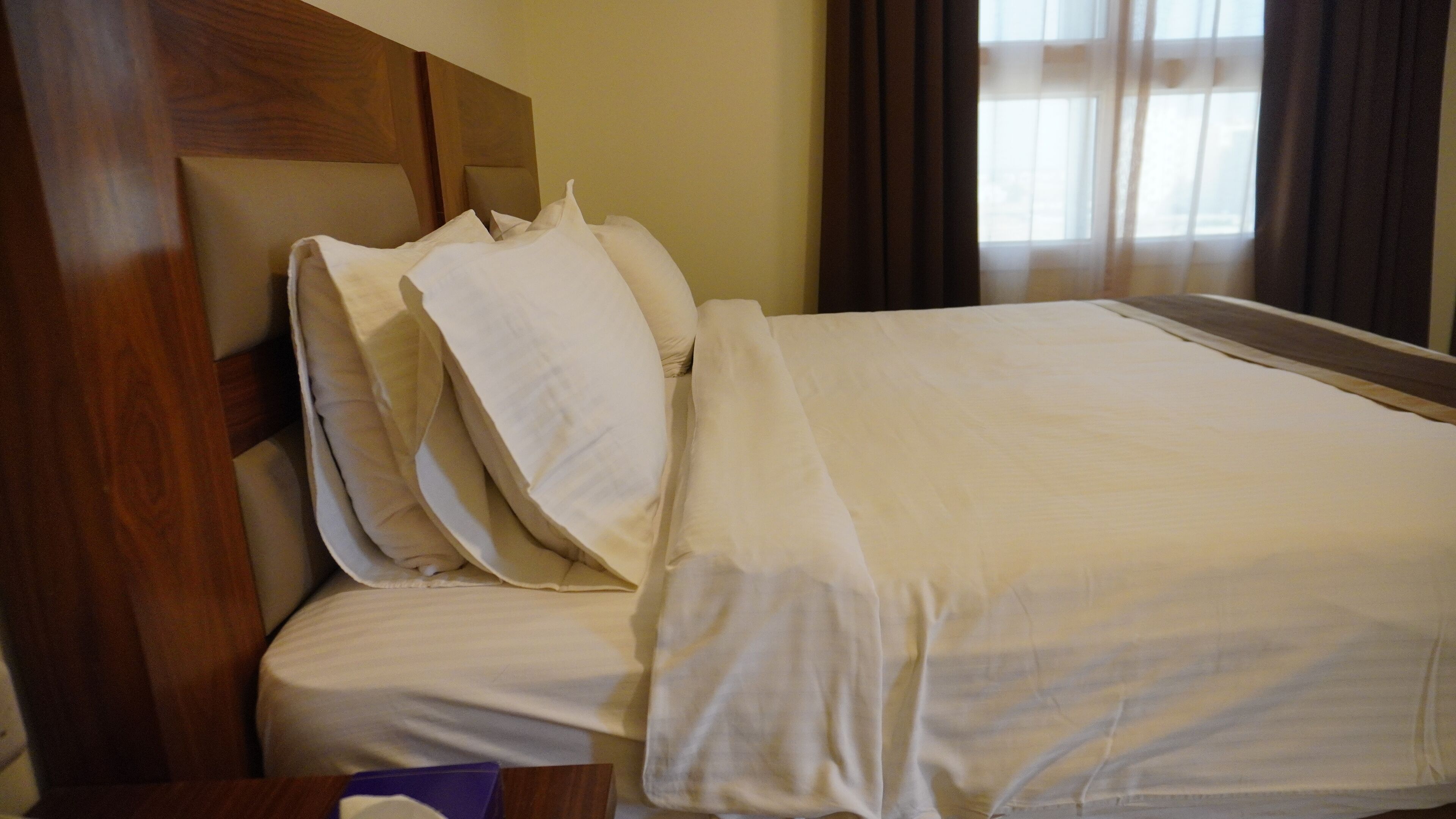 Un lit bien fait, avec du linge de lit blanc et une tête de lit en bois, dans une chambre d’hôtel.