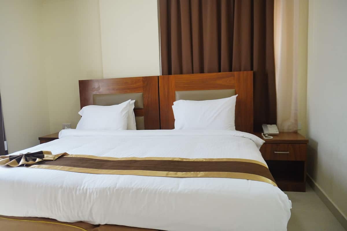 Habitación de hotel con una cama grande, cabecera de madera, dos mesitas de noche y un teléfono en una de ellas.