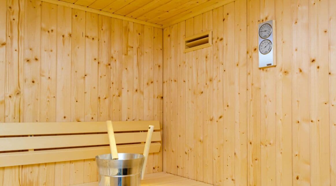 A sauna room with wooden walls, a bench, and a bucket with a ladle.