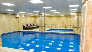 Una piscina interior con carriles delimitados, suelo de baldosas y sillones de descanso a lo largo de la pared.