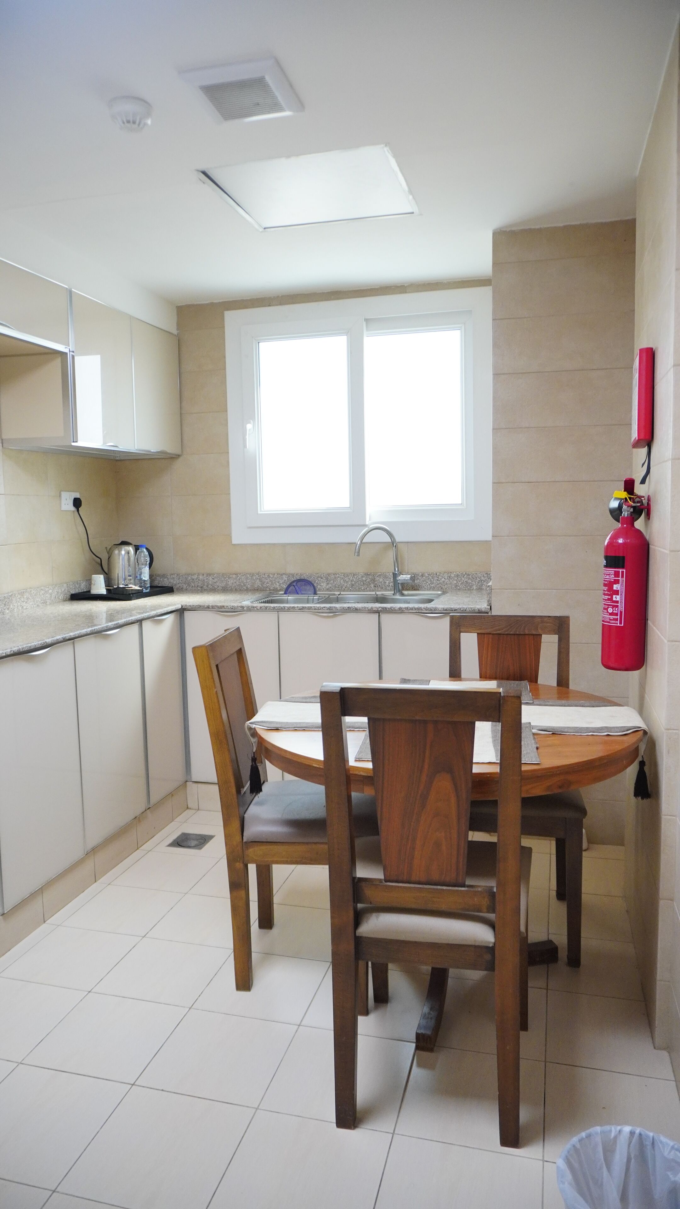 A kitchen with a dining table, chairs, a window, a sink, and a fire extinguisher.