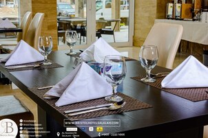 Un restaurante con una mesa lista para cuatro, incluyendo servilletas blancas, copas de vino y cubiertos. La mesa está en un moderno comedor con vista a la calle.