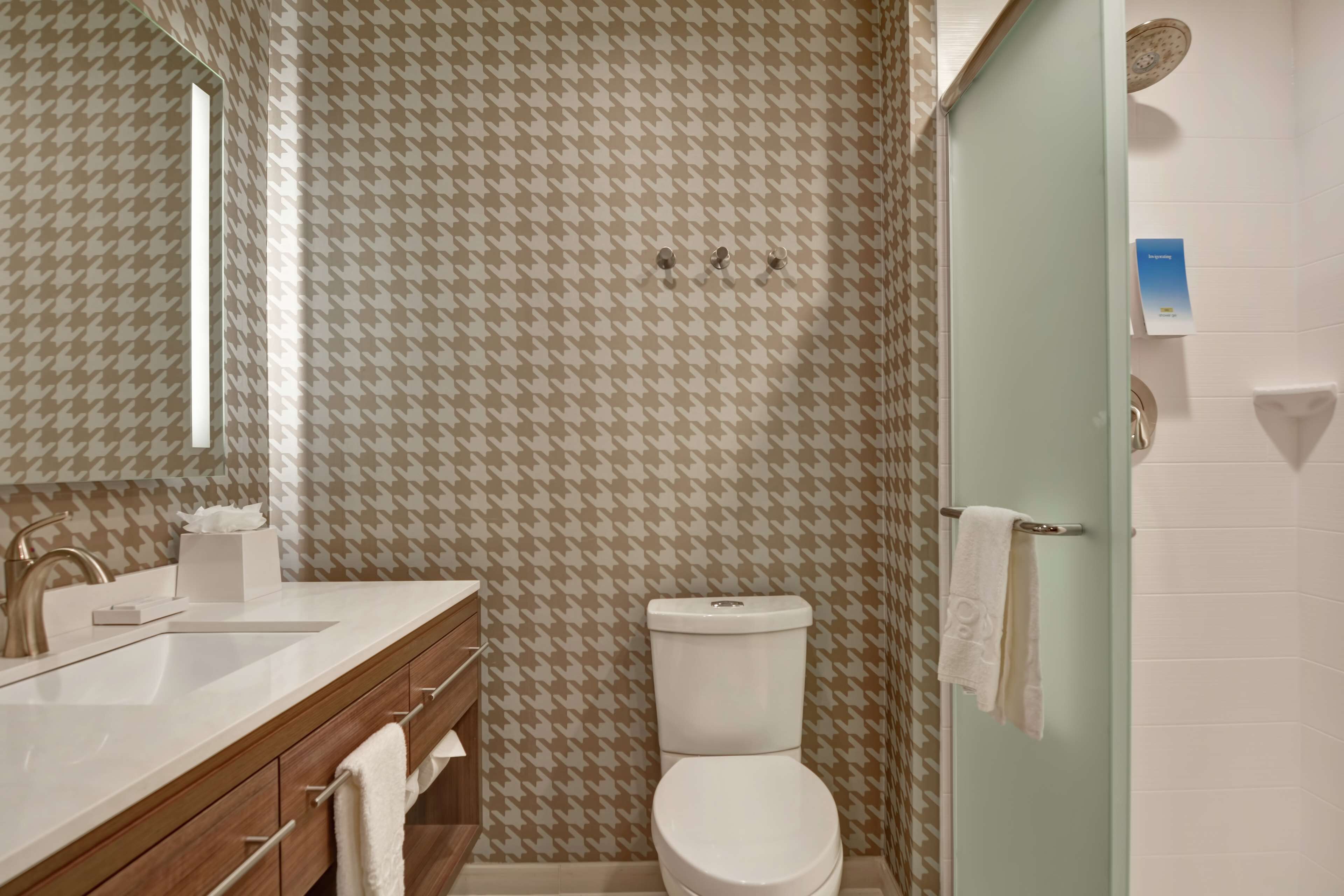 Un baño con pared de estampado pata de perro, un inodoro blanco, un lavamanos con espejo y un perchero para toallas.