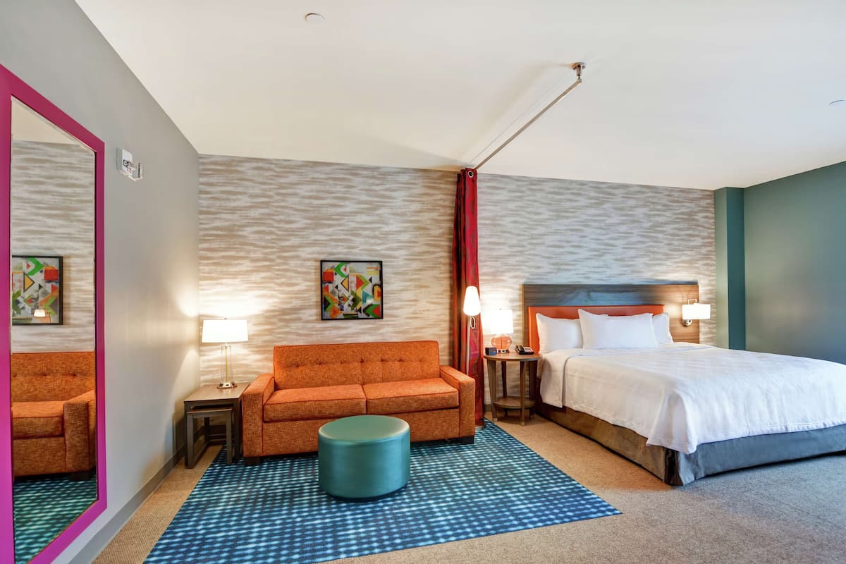 Ein Hotelzimmer mit einem Bett, einer Couch, einem kleinen Tisch, einer Lampe und einem Spiegel.