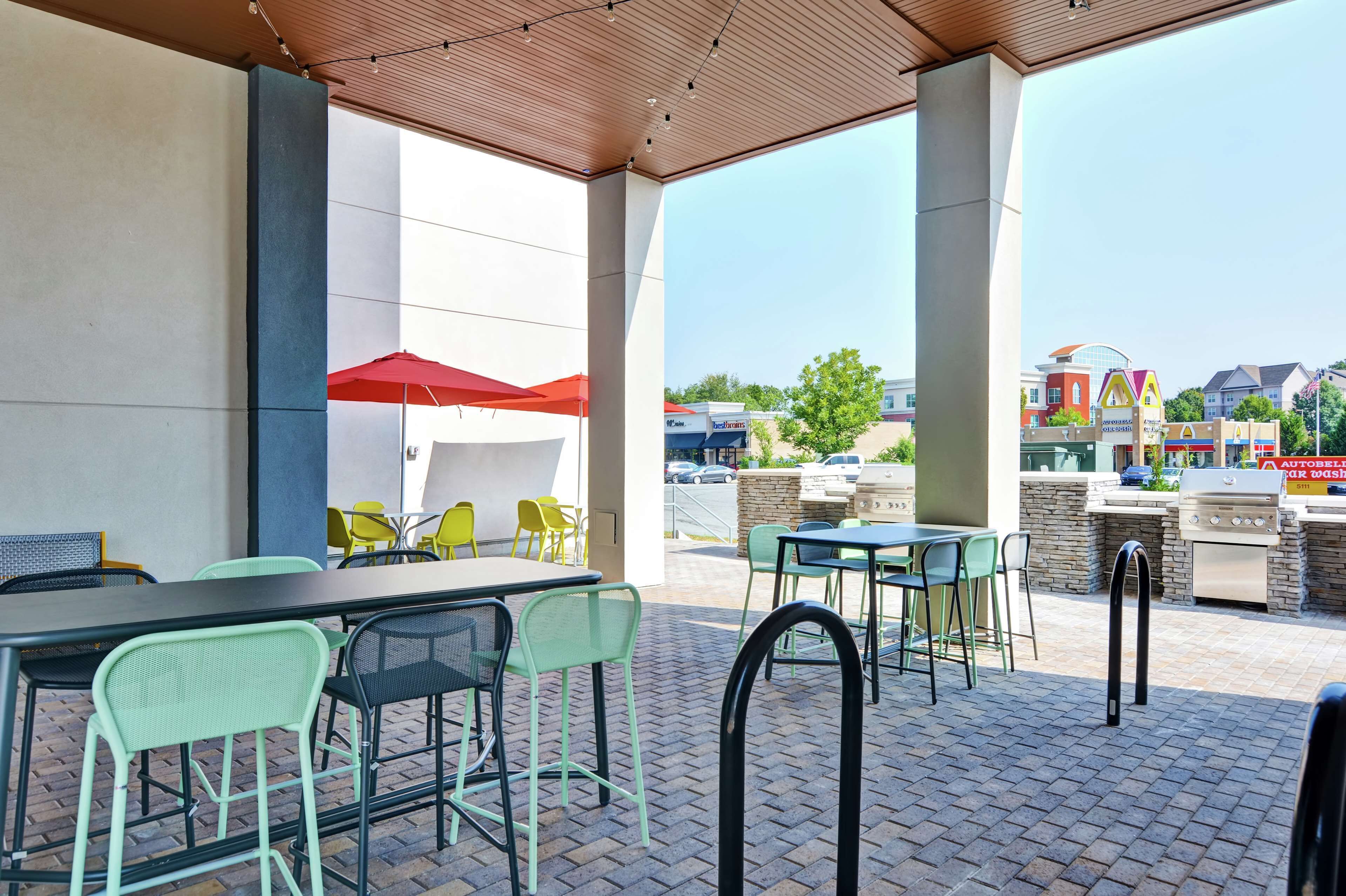 Une terrasse extérieure avec des tables et des chaises, un barbecue et un parasol rouge.