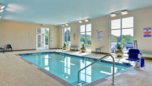 An indoor swimming pool with clear glass walls, a lifeguard chair, and a bench.
