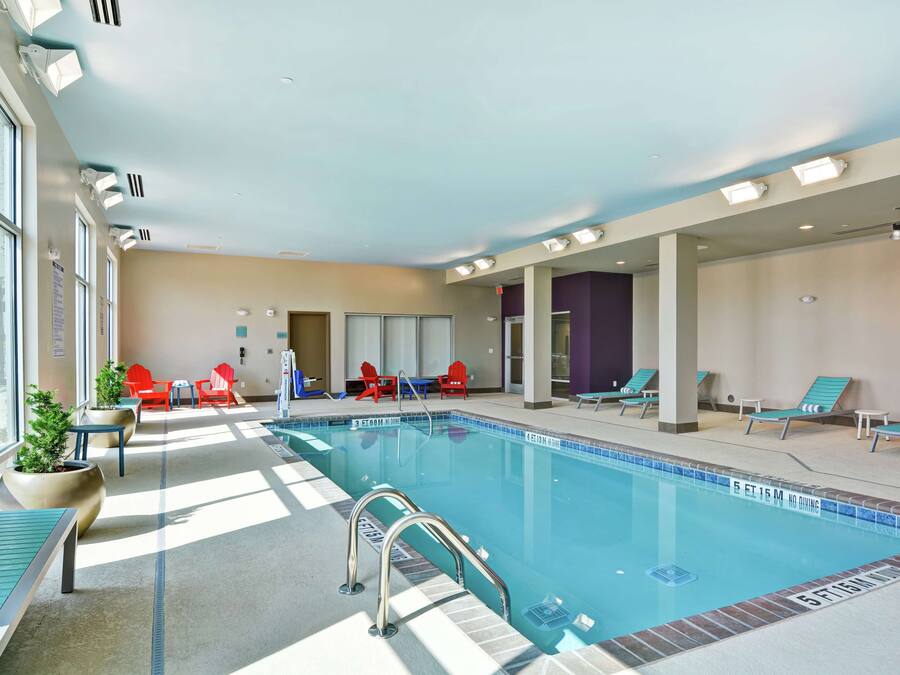 An indoor swimming pool with clear blue water, surrounded by lounge chairs and potted plants.