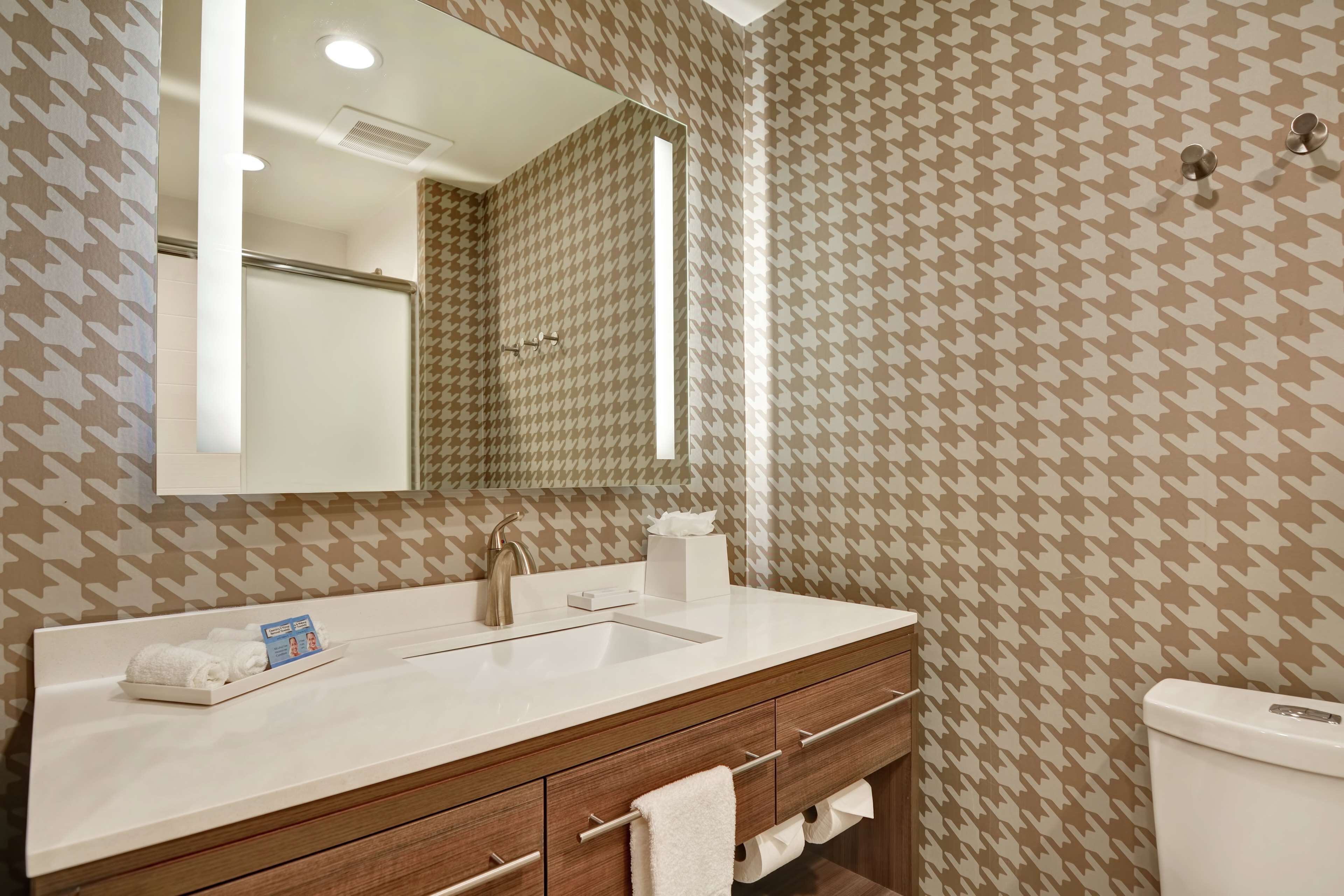 A bathroom with a patterned wallpaper, a sink with a mirror, a towel rack, and a toilet.