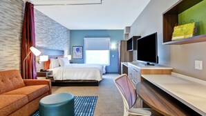 A hotel room with a bed, a desk, a TV, a sofa, and a chair.