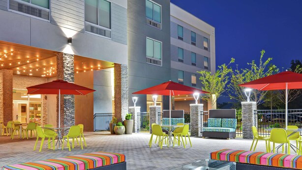 An outdoor patio area with yellow chairs and red umbrellas, a glass-top table, and a stone wall.