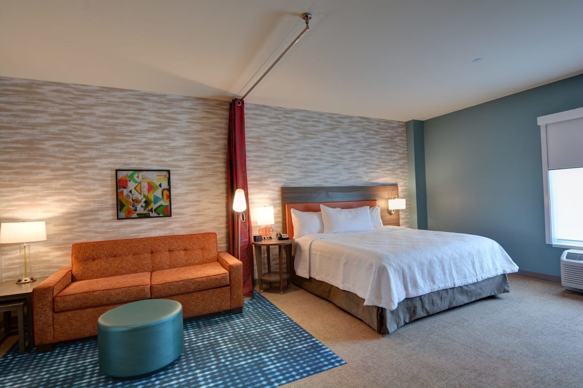 Ein Hotelzimmer mit einem Bett, einem Sofa, einem kleinen Tisch, einer Lampe und einem Wandbild.