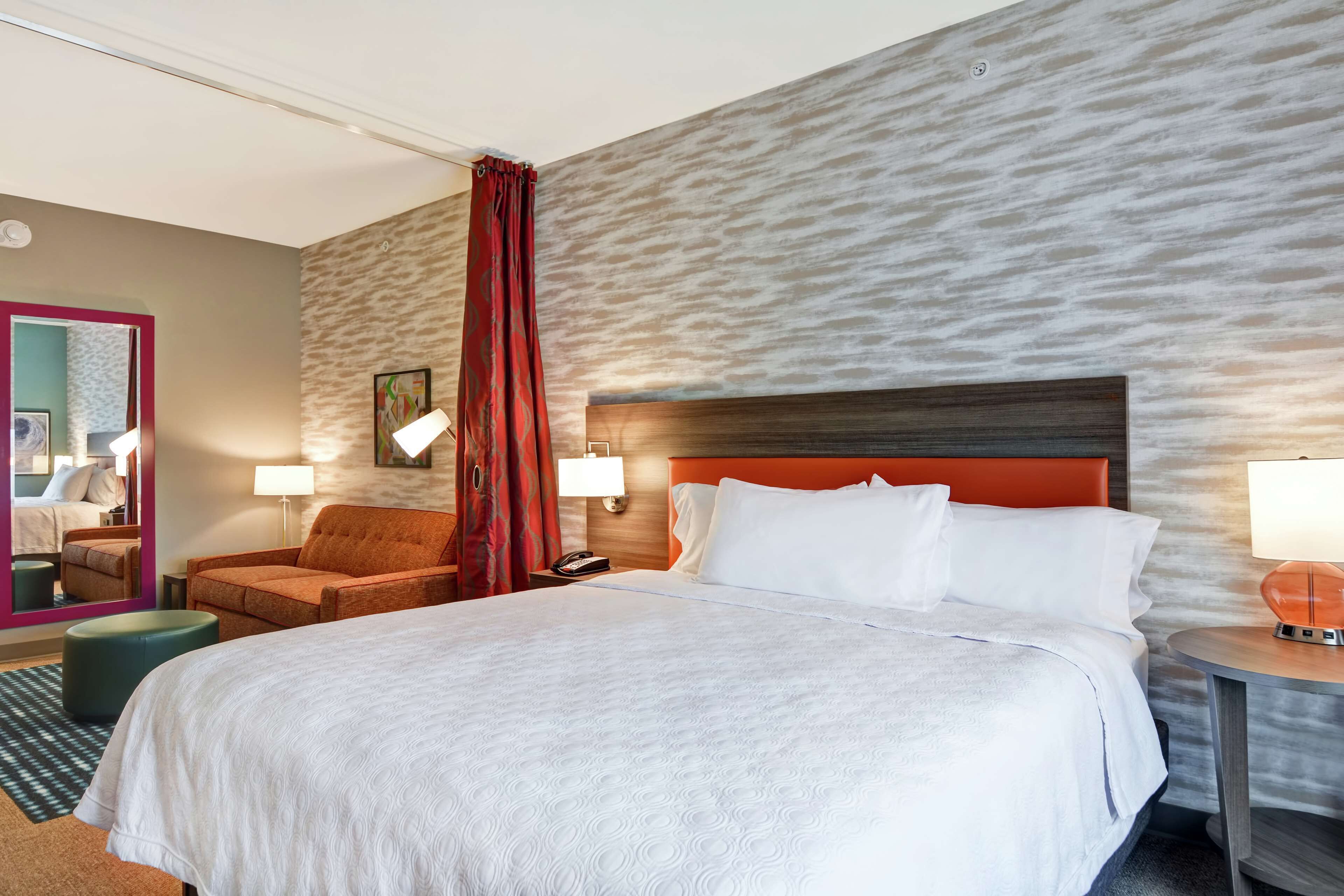 A hotel room with a large bed, a red curtain, a wooden headboard, and two bedside lamps.