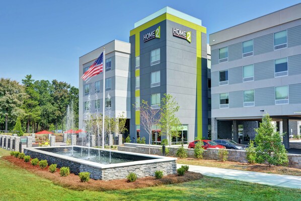 A modern hotel with a fountain, outdoor seating, and a parking area.