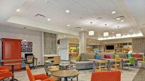 A modern hotel lobby with seating areas, a reception desk, and a dining area.