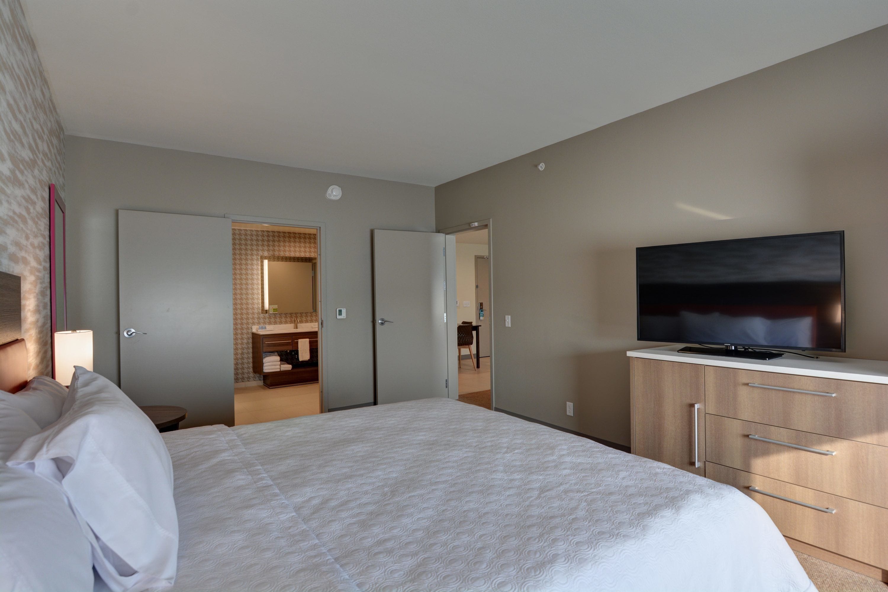 Camera d'albergo con un grande letto, una televisione su un mobile e un bagno visibile attraverso una porta aperta.