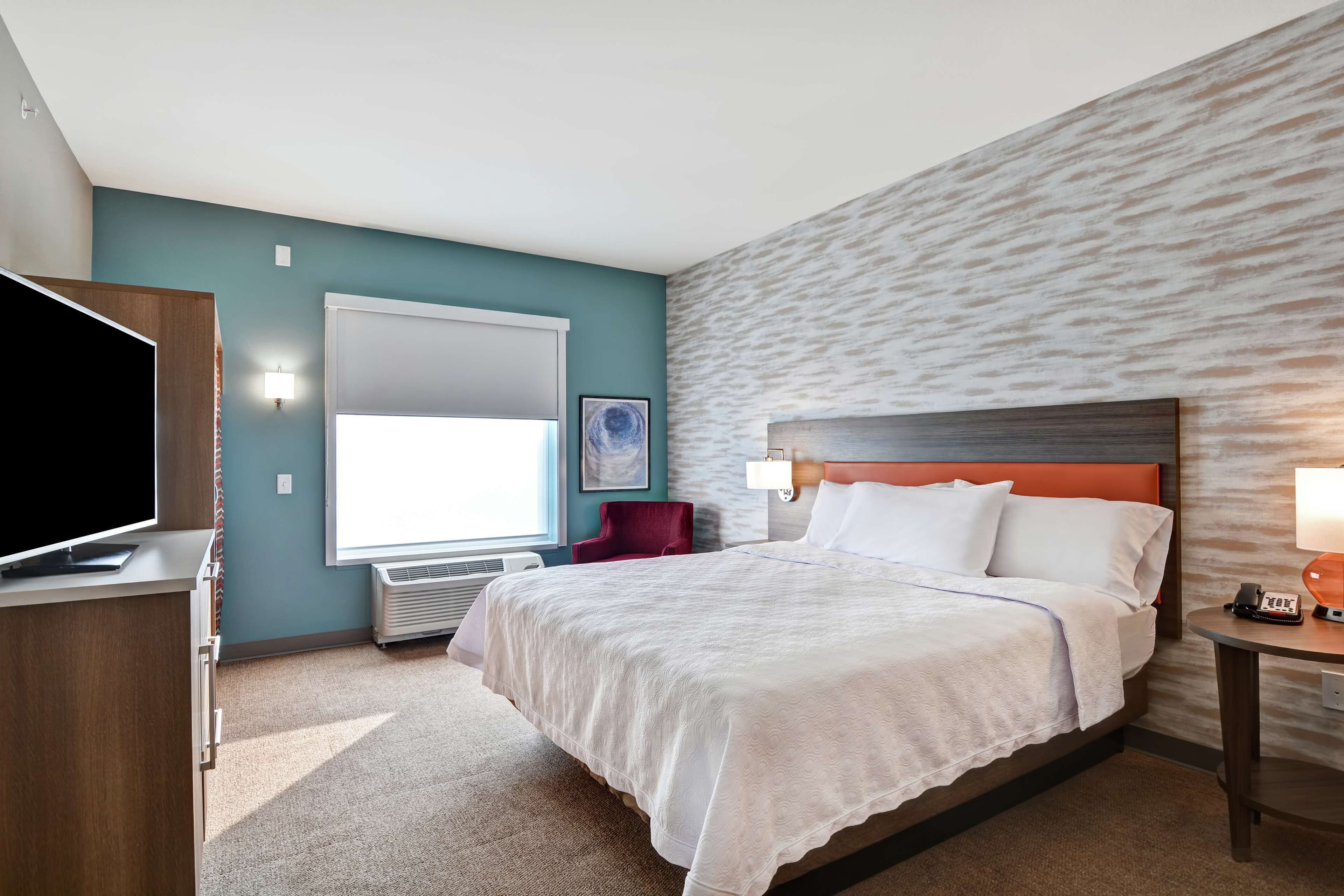 Habitación de hotel con una cama grande, televisor, escritorio y ventana con persianas.