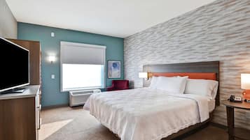 Habitación de hotel con una cama grande, televisor, escritorio y ventana con persianas.