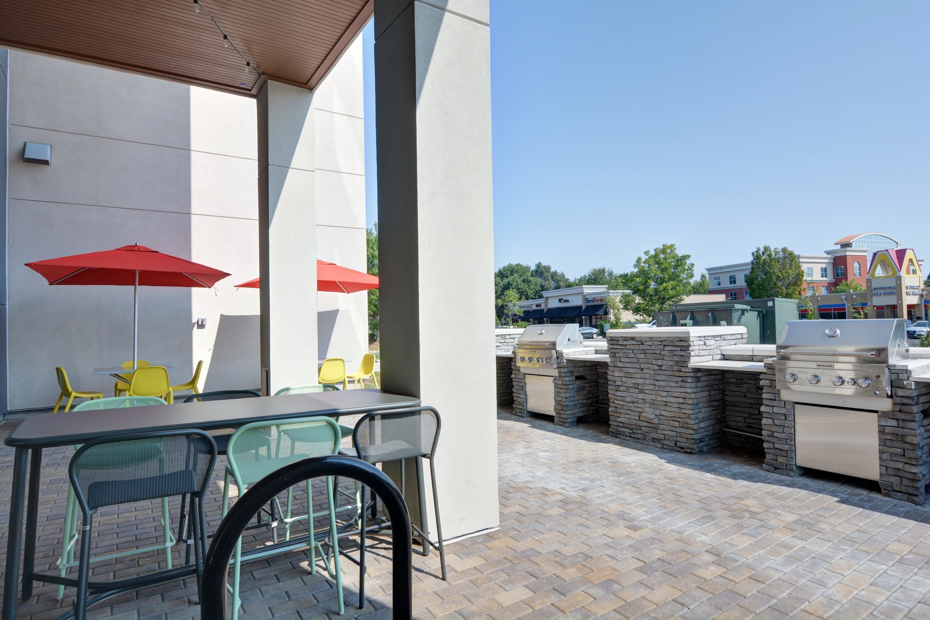 An outdoor patio with a table and chairs, red umbrellas, and a barbecue grill area.