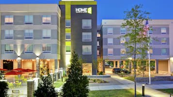Un hotel moderno con un cartello ben visibile 'HOME 2', area salotto esterna e un ingresso illuminato.
