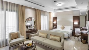 Habitación de hotel con cama, sofá, sillón, escritorio y una mesa redonda con fruta.