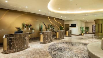 A hotel reception area with marble counters, a curved ceiling, and potted plants.