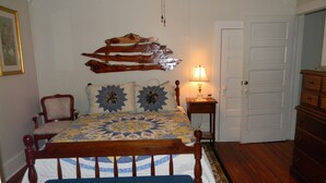 Un dormitorio con una cama de madera, una silla, una mesita de noche con una lámpara, una puerta y un aparador.