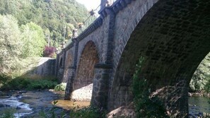 Un puente de piedra sobre un río, con un paisaje boscoso al fondo.