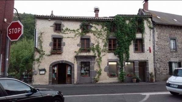 A stone building with ivy, a stop sign, and a car parked in front. - Hotel des Voyageurs (Ferrières-Saint-Mary)