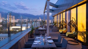 A rooftop dining area with a table set for four, overlooking a cityscape and mountains.