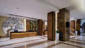 A modern reception area with a wooden reception desk, a large tree mural, and a staircase leading to upper floors.