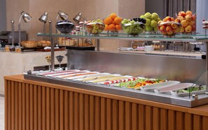 A buffet with various fruits and vegetables, including apples, oranges, and grapes, arranged on a glass counter. - DoubleTree by Hilton Almaty (Almaty)